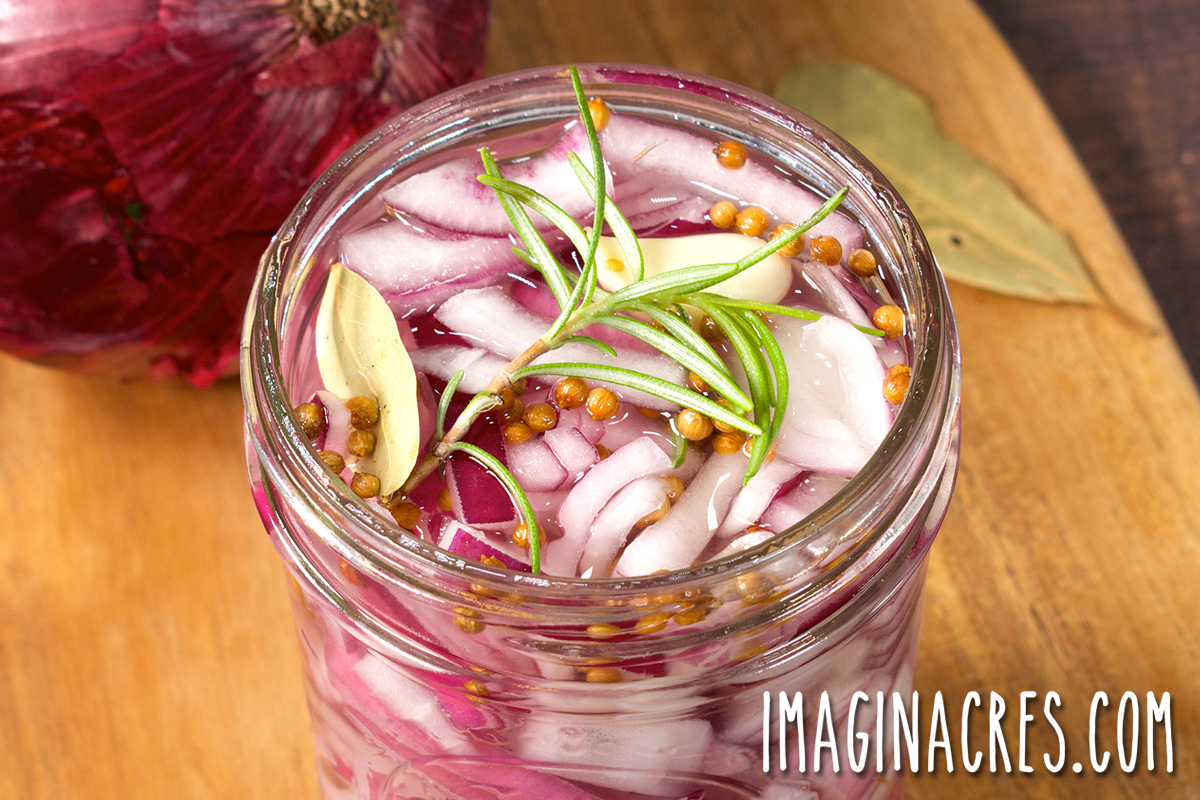 An open jar of pickled onions with dried spices and rosemary.