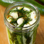 An open jar of zucchini pickle spears with dill, garlic, and spices on a table.